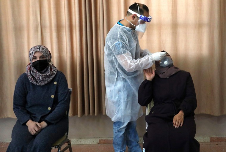 Image: A Palestinian health worker takes a swab sample from a woman to test for Covid-19 in the West Bank village of Dura, southwest of Hebron