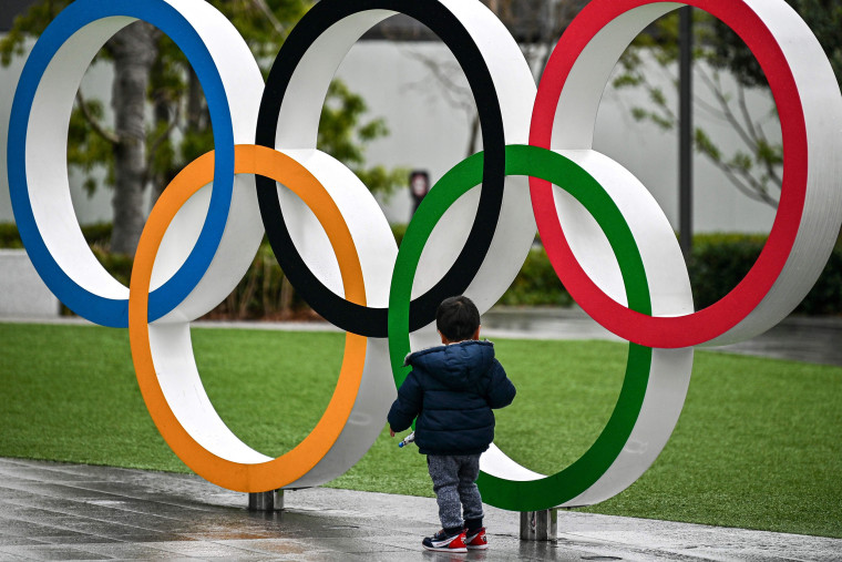 Image: A child stands next to the Olympic rings outside the Japan Olympic Museum in Tokyo
