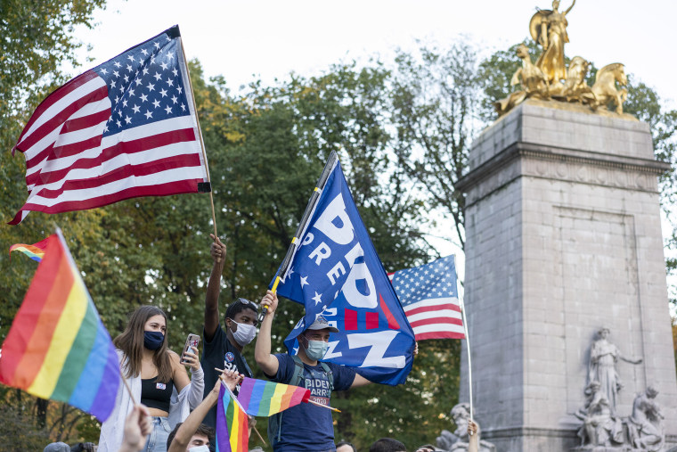 Image: People wave Biden for President, LGBTQ, and American flags near Columbus Circle.