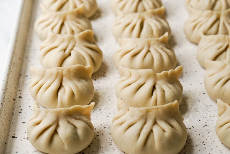 Classic dumplings with the yuan ban fold sit on a tray before being cooked.