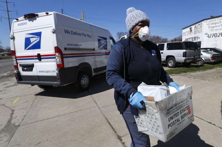 Image: A United States Postal worker makes a delivery with gloves and a mask in Warren, Mich