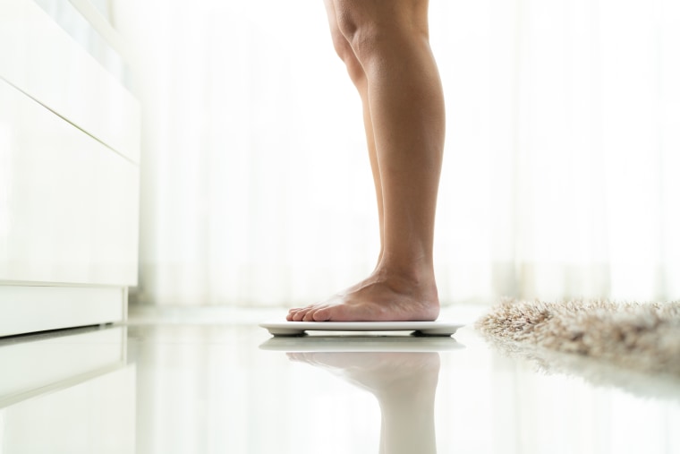 Low Section Of Woman Standing On Electronic Weight Scale On Floor