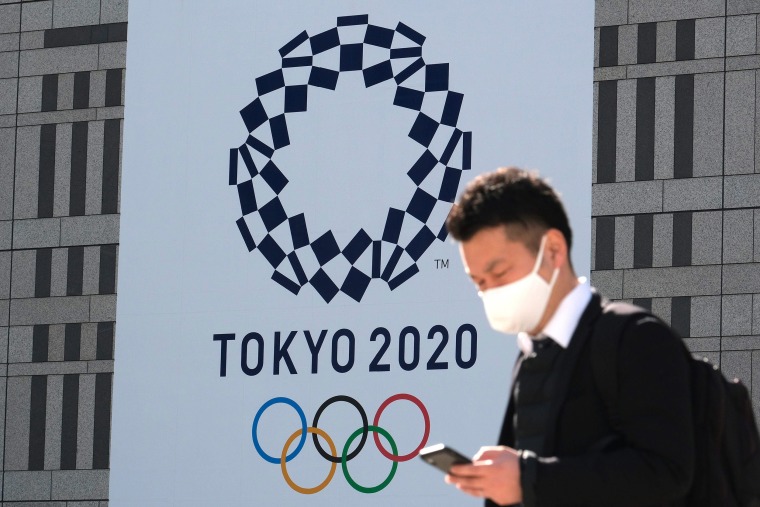 Image: A pedestrian walks past the logo of the Tokyo 2020 Olympic displayed on a wall of the Tokyo Metropolitan Government building in Tokyo