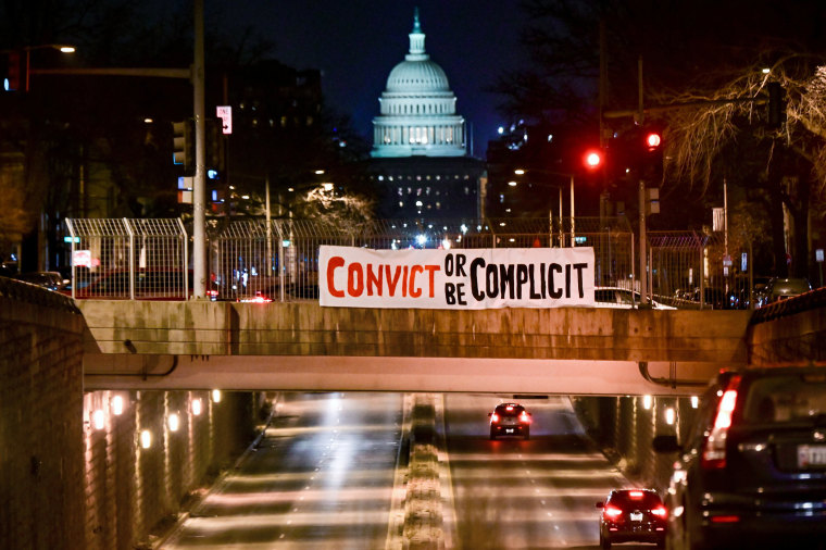 Image: A banner reading, "Convict or be complicit" is hung over a bridge in view of the U.S. Capitol