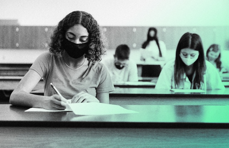 Image: Stock photo of high school-aged students wearing masks take a test.