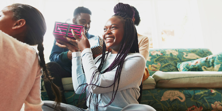 Low angle view of excited girl holding  present while sitting with sister in living room