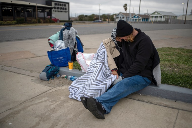 Image: Couple sit amongst belongings as they embrace to keep warm in Galveston, Texas