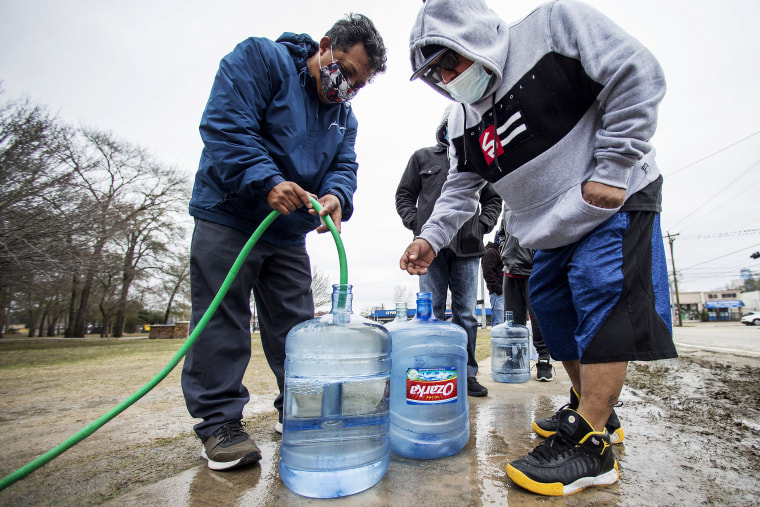 Image: Victor Hernandez, left, and Luis Martinez fill their water containers with a hose from a spigot in Haden Park