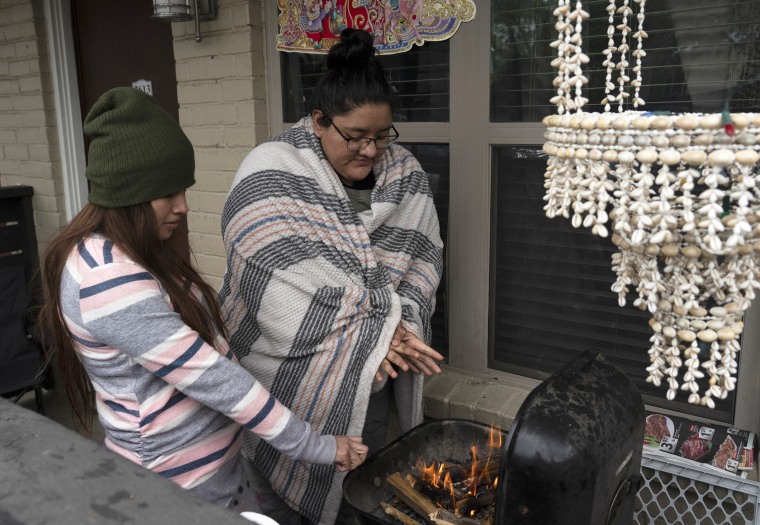 Image:  Karla Perez and Esperanza Gonzalez warm up by a barbecue grill during the power outage