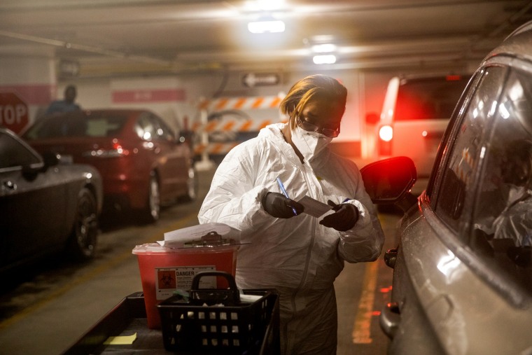 IMage: A nurse speaks with a person in their vehicle waiting to receive the Covid-19 vaccine in Detroit on Jan. 15, 2021.