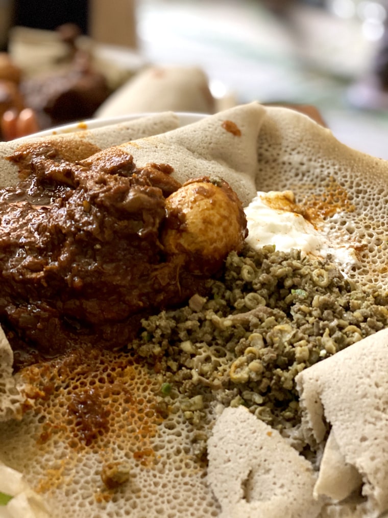 A photo of Doro Wot and Dulet with a side of sour cream accompanies an article called "Cooking in the Motherland" by Hirut Haleff.