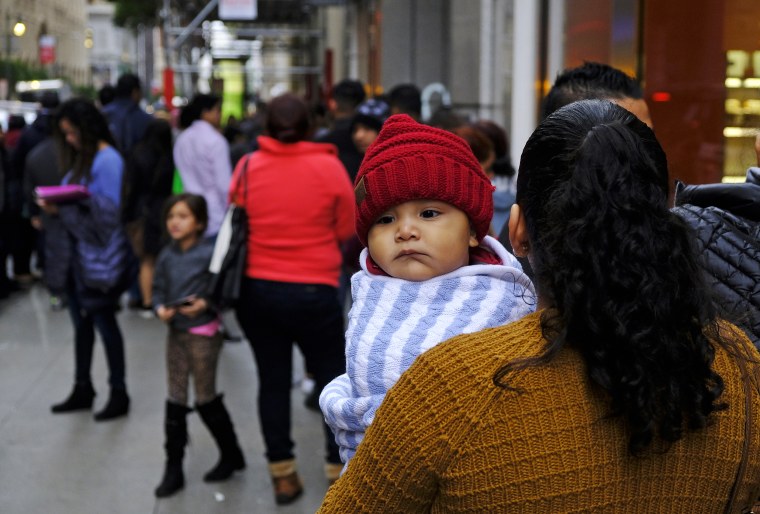 A woman holds a child in a line snaking around the block outside a U.S. immigration office on Jan. 31, 2019, in San Francisco.