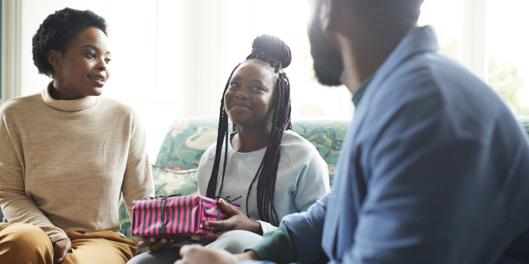 Teenage girl holding gift sitting on sofa at home