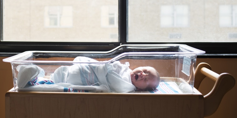 Baby boy yawning while sleeping in crib by window at hospital