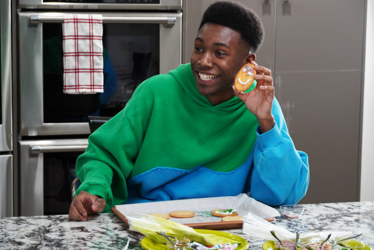 young man in hoodie smiles holding a cookie next to his face