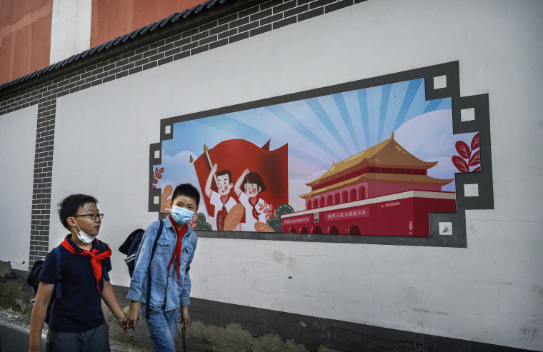 Image: Chinese boys pass a patriotic banner as they walk home together from a local elementary school after classes