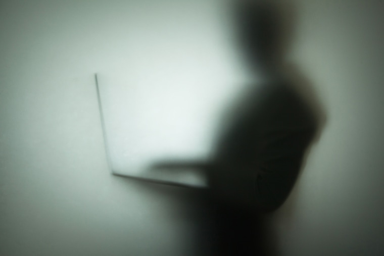 Silhouette of person using laptop, behind glass