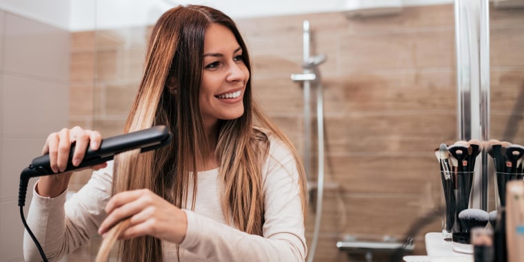 Woman straightening her hair in the bathroom with her hair iron
