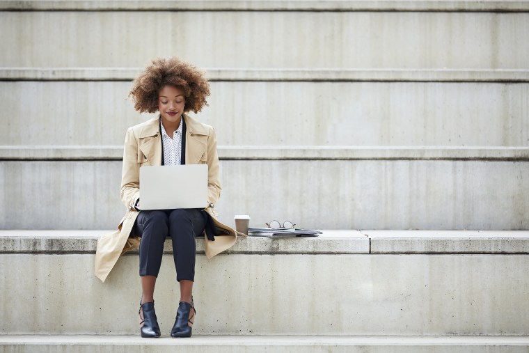 Young businesswoman using laptop while sitting on steps. Full length of female professional working on staircase. She is wearing long winter coat.