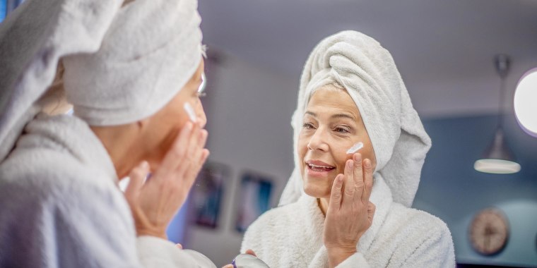 Woman rubbing anti aging eye cream while looking at herself in the bathroom