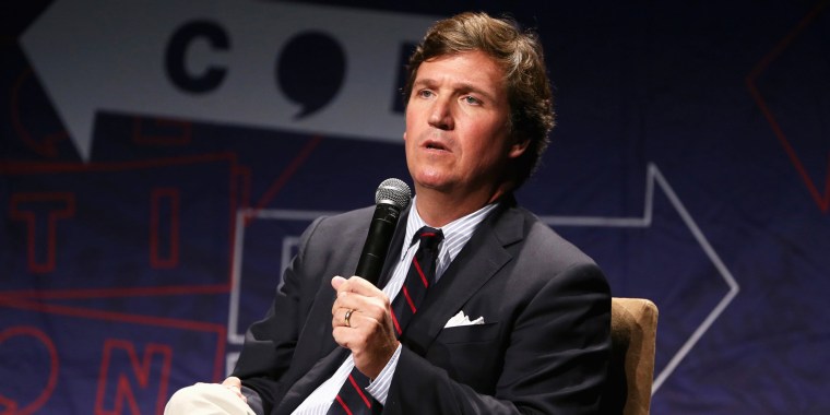 tucker carlson reclines in a chair with a microphone
