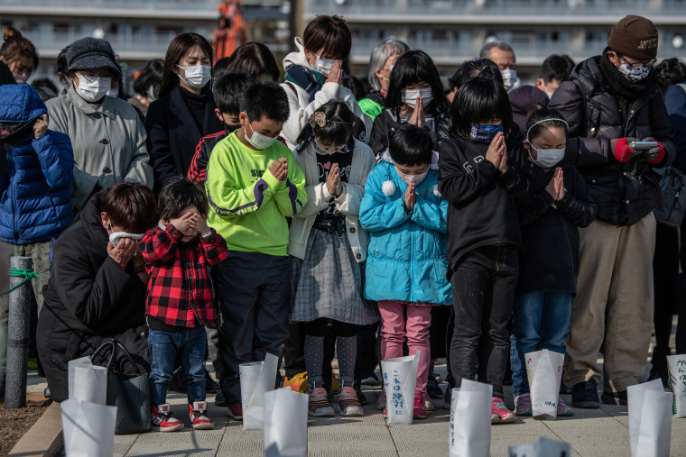 Image: A woman and child cover their eyes as others pray during a minute of silence to mark the 10th anniversary of the 2011 Tohoku earthquake and tsunami