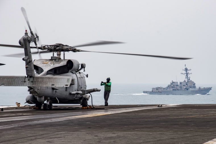Image: Aviation Electronics Technician 3rd Class James Benzel signals an MH-60R Sea Hawk to disengage its rotors on the flight deck of the USS Ronald Reagan (CVN 76) as USS Mustin (DDG 89) steams alongside in South China Sea