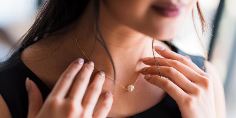 Close up image of a Woman touching a beautiful gold-chained necklace with a single pearl