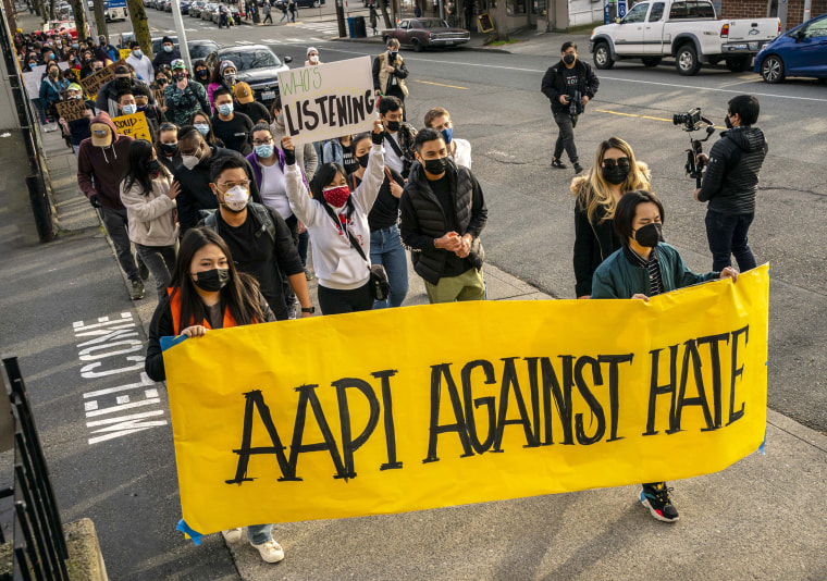 Demonstrators walk in the street with a bright yellow banner that reads "aapi against hate"