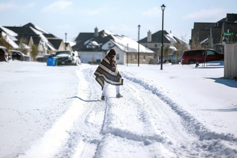 Image: A man walks to his friend's home in a neighbourhood without electricity as snow covers the BlackHawk neighborhood in Pflugerville