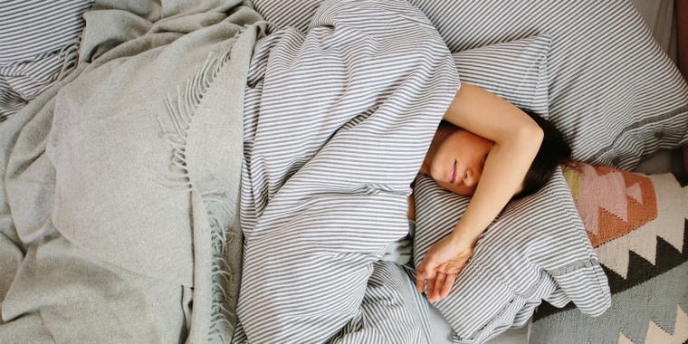 Woman sleeping in her bed under a grey-striped down duvet blanket