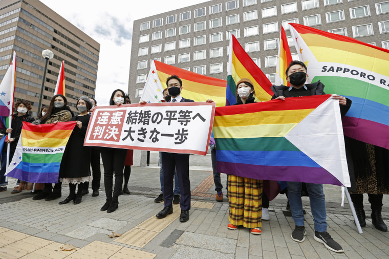 Image: Plaintiffs' lawyers and supporters hold rainbow flags and a banner that reads: \"Unconstitutional judgment\" outside Sapporo District Court after a court rule, in Sapporo, northern Japan
