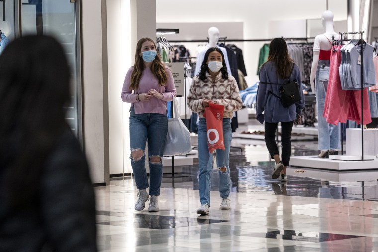 Image: Shoppers wearing protective masks carry bags inside a shopping mall in San Francisco on March 9, 2021.