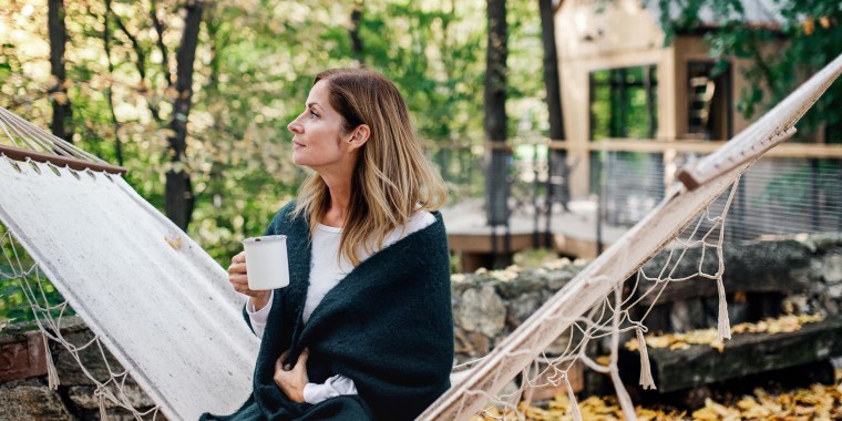 Woman sitting outside on her hammock, in her backyard, drinking tea. Best hammock sales of 2021 include Wayfair, Walmart, Amazon and more. Shop the best hammocks at a discount before summer starts.