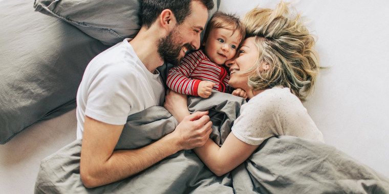 Mom and dad hugging their baby in bed, under the blanket