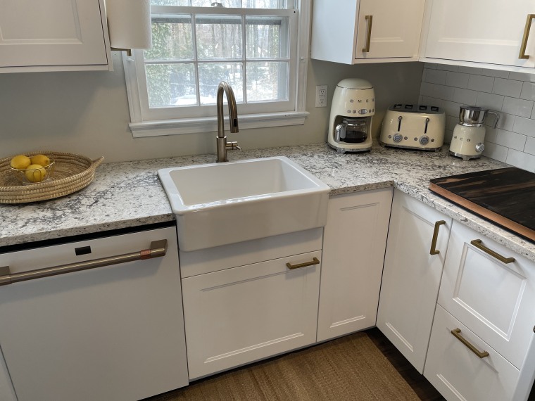 A farmhouse sink, small Smeg appliances and a hand-woven fruit basket bring organic texture and some vintage aesthetic to the modern white kitchen.