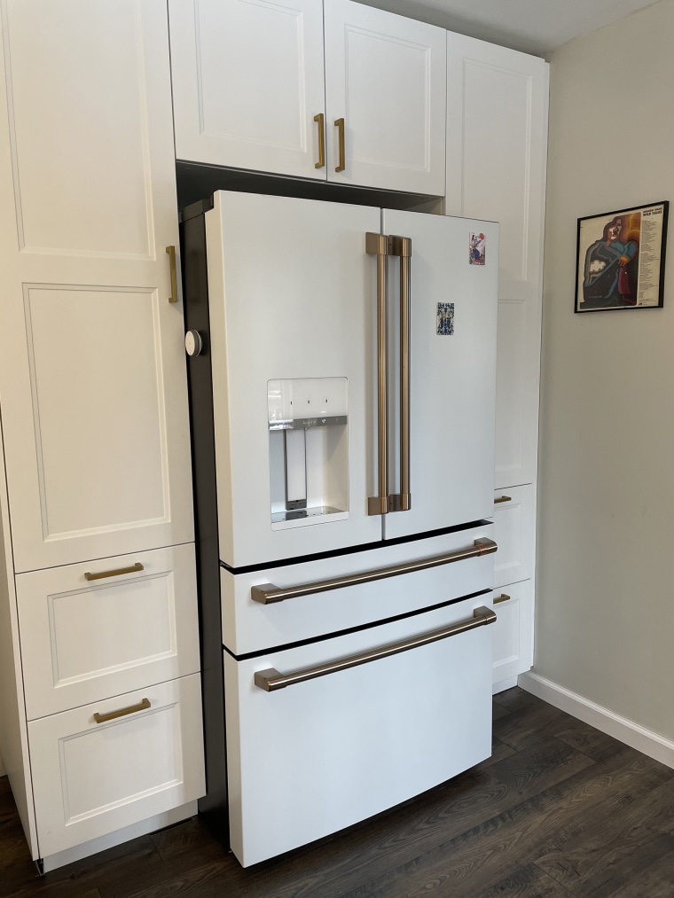 The French Door refrigerator from Cafe in white with brushed bronze accents flows effortlessly with the built-in pantry surrounding it. 