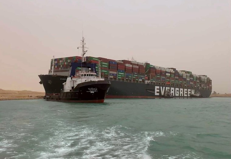 Image: A boat navigates in front of a massive cargo ship, named the Ever Given, rear, sits grounded