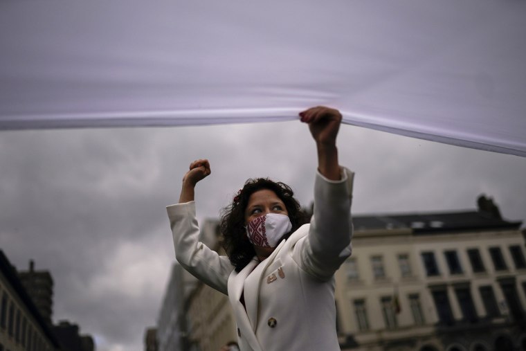 Image: An opposition supporter holds a giant Belarus historical flag as she shouts slogans during a protest outside the European Parliament in Brussels.