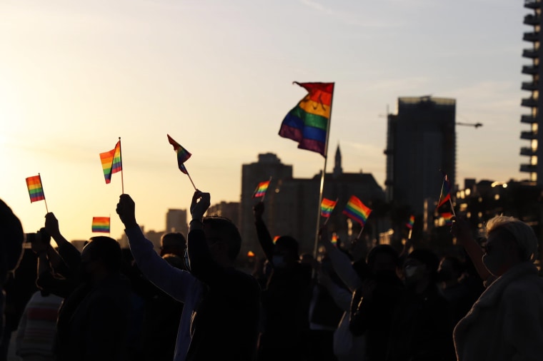 People wave pride flags at a rally in Long Beach, Calif., on March 24, 2021, after an LGBTQ lifeguard tower burned down the day before.