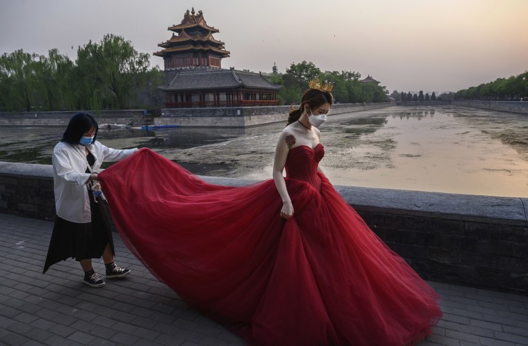 Image: A Chinese woman wears a protective mask as she is helped by a photo assistant while taking pictures in advance of her wedding outside the Forbidden City,