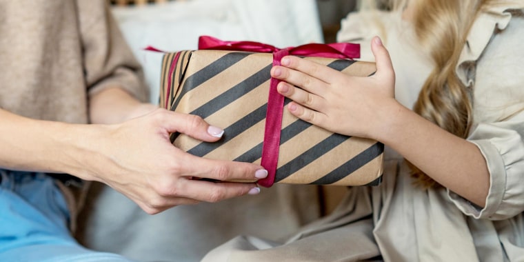 Woman handing her daughter a box wrapped in striped black and brown wrapping paper and a red ribbon