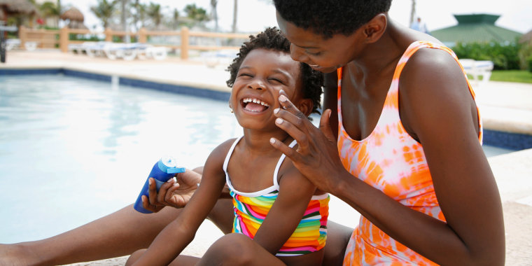 Woman applying kids sunscreen to childs face sitting by pool. The best sunscreens for kids that are dermatologist recommended. Get the best sun protection for your kids from Neutrogena, Aveeno, Baby Bum and more.