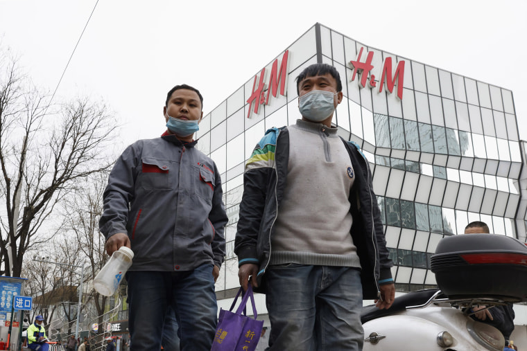 Image: Workers wearing masks pass by an H&amp;M store in Beijing