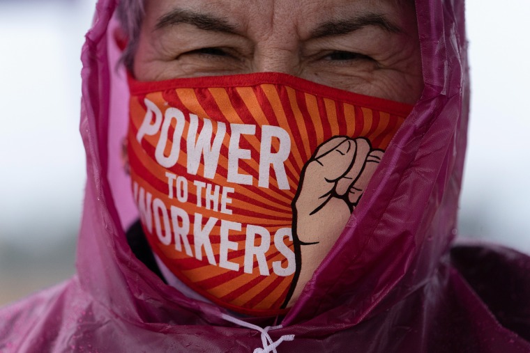 Image: A demonstrator's mask reads "Power To The Workers" 