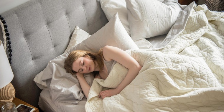 Woman sleeping in her bed, surrounded by 4 white fluffy pillows. Shop the best bed pillows of 2021 including memory foam pillows and pillows that support your back and neck from Buffy, Casper, Brooklinen, Beckham and more.