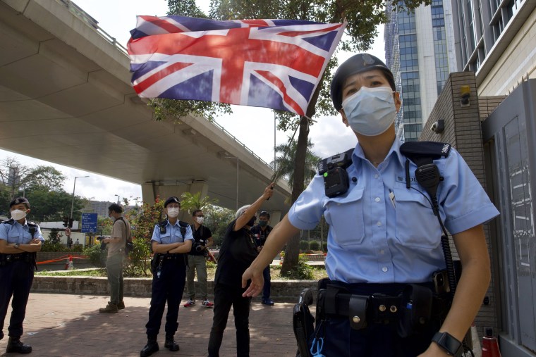 A pro-democracy supporter waves a British flag as police officers stand guard outside a court in Hong Kong Thursday, April 1, 2021.