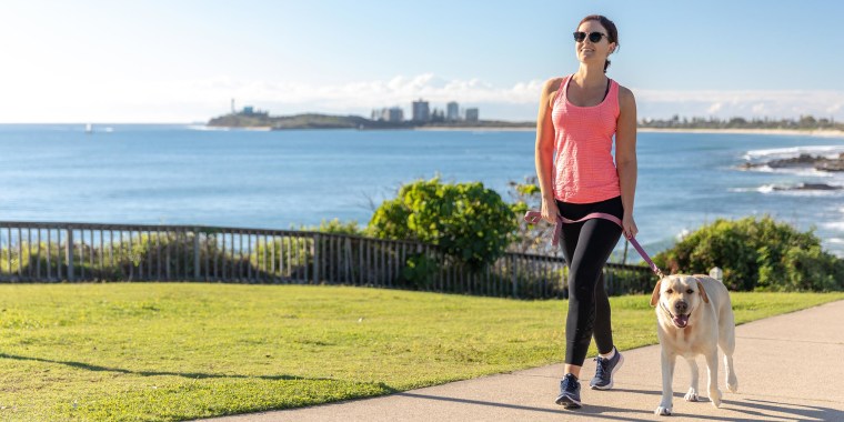 Woman wearing black leggings and a pink tank, walking her dog outside