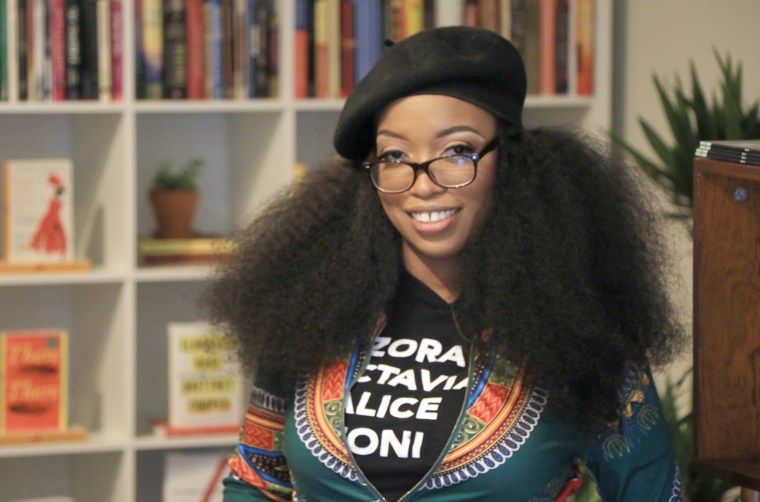 Under an Ankara print jacket, Cook wears a shirt featuring names of Black women authors, such as Zora Neale Hurston, Octavia Butler, Alice Walker and Toni Morrison.
