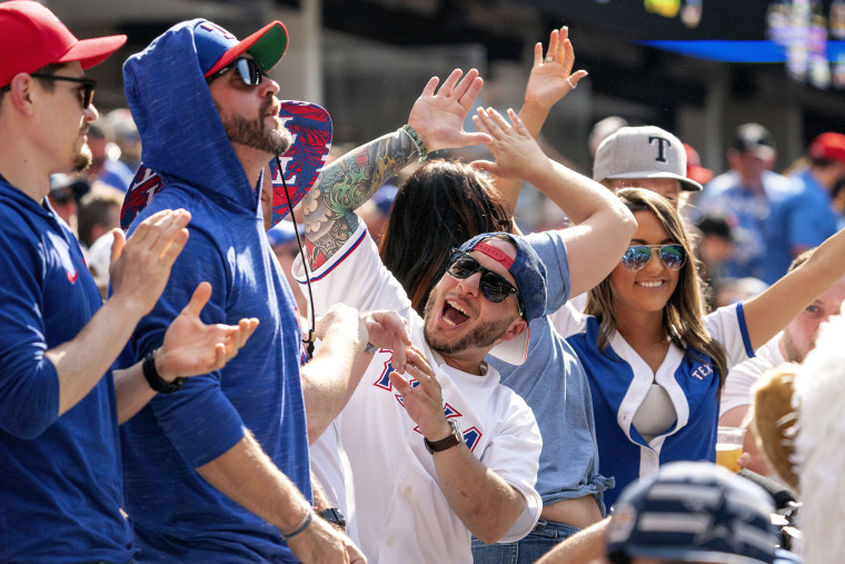 Image: A Texas Rangers fan celebrates with friends during the fourth inning of a baseball game against the Toronto Blue Jays on April 5, 2021, in Arlington, Texas.